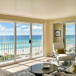 Oceanfront condo with balcony overlooking turquoise water and beach.